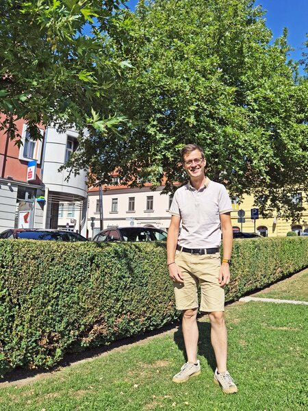 Mann mit Brille und beiger Kleidung steht vor einer Hecke in Graz
