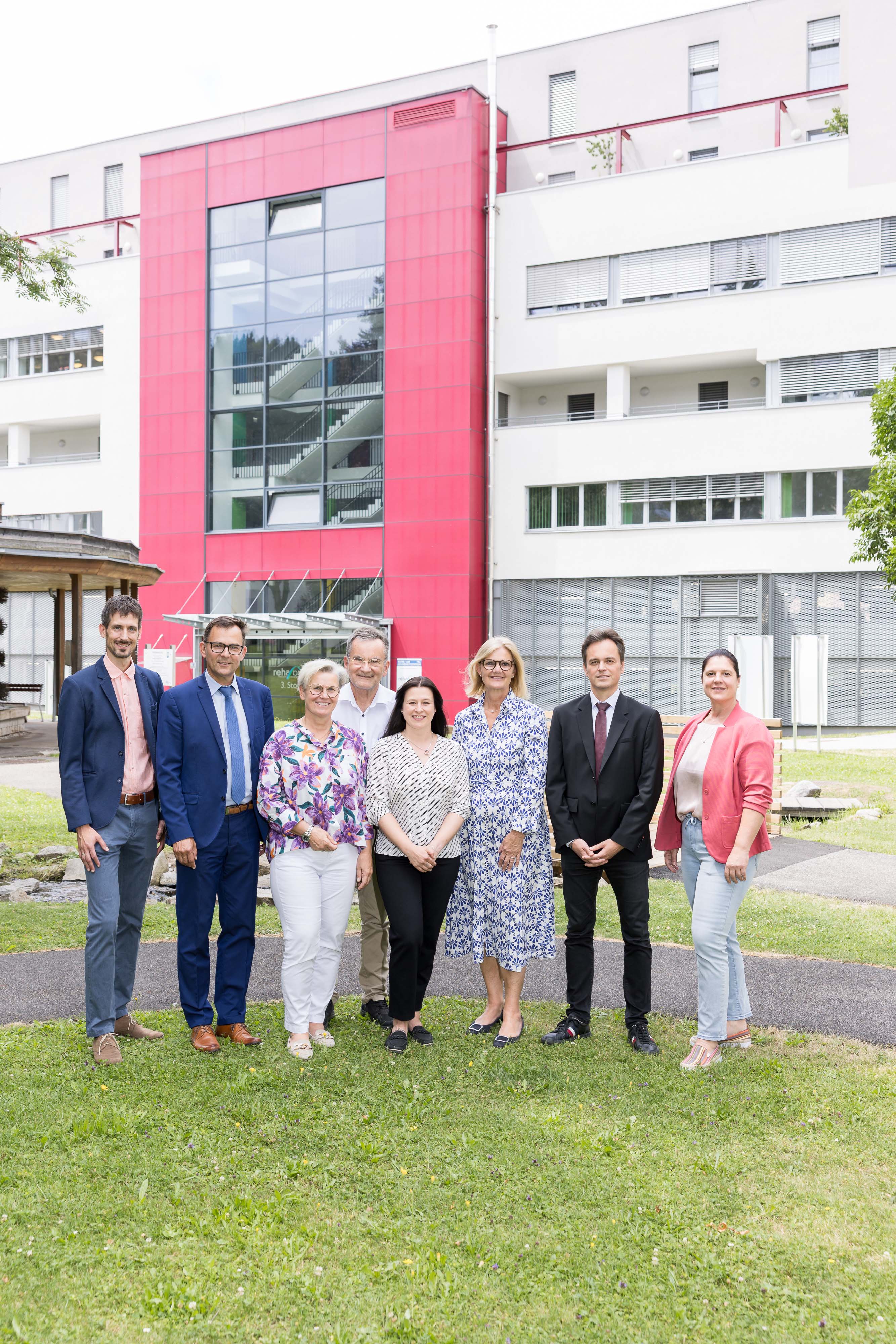 Teamfoto vor moderner Architektur in Österreich mit Personen in Anzügen und Kleidern.