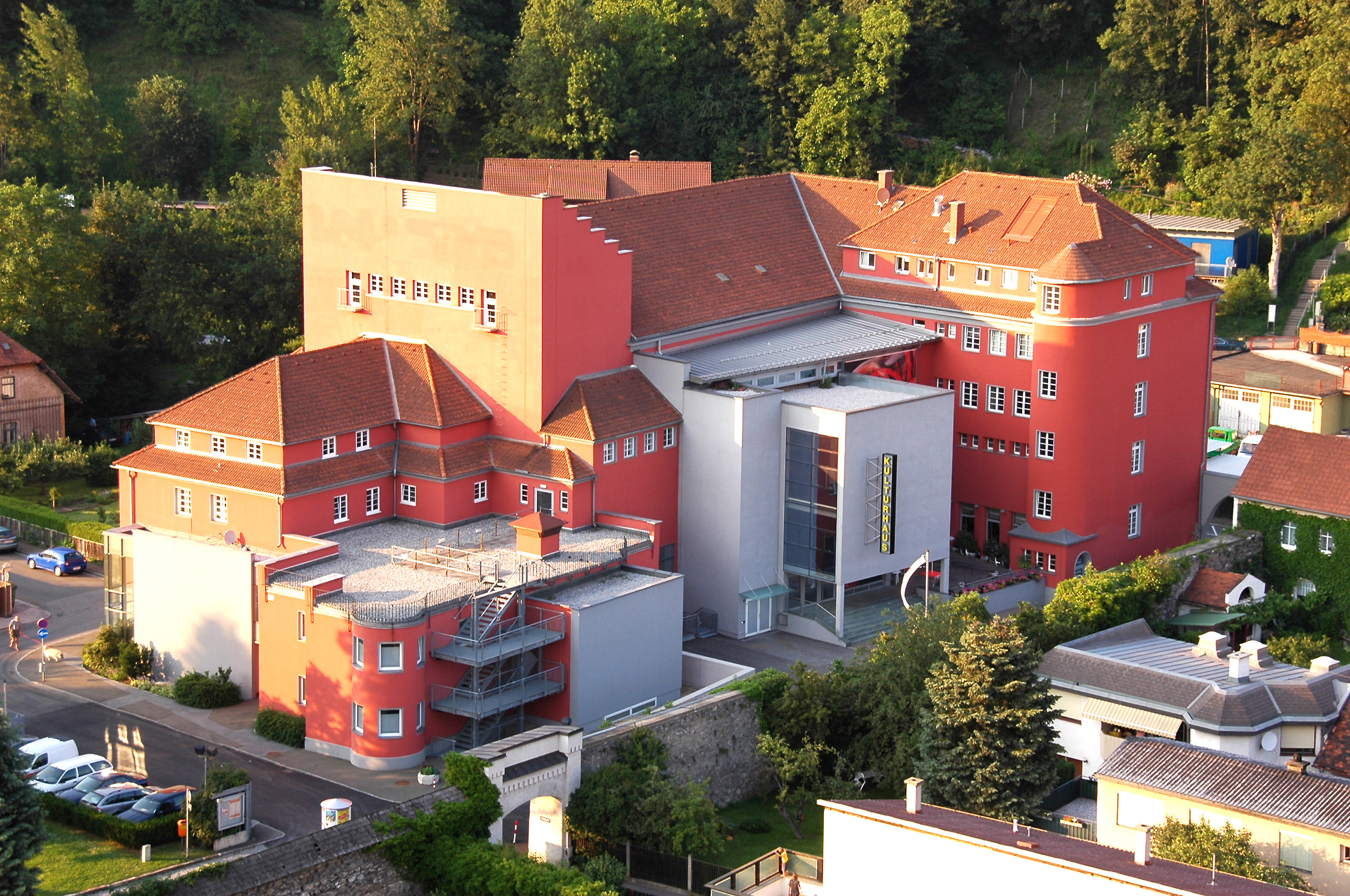 Kulturhaus in Gmunden mit roter Fassade und moderner Glasfront, umgeben von Bäumen.